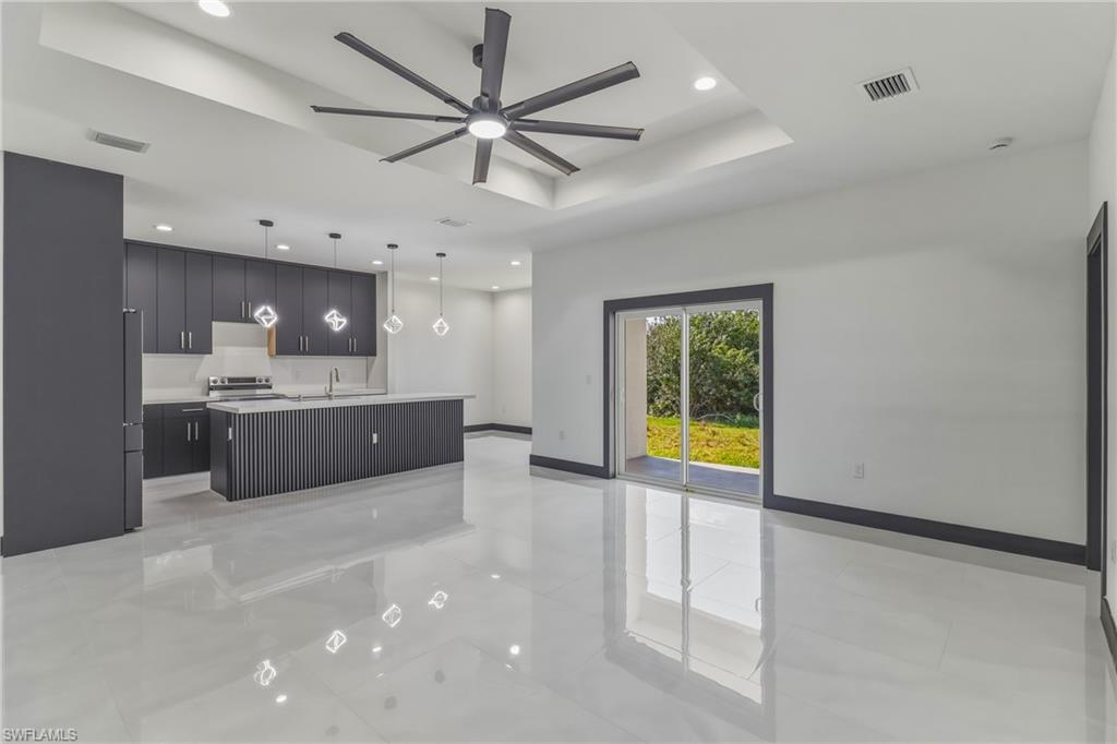 Kitchen with a center island with sink, light countertops, a tray ceiling, pendant lighting, and open floor plan