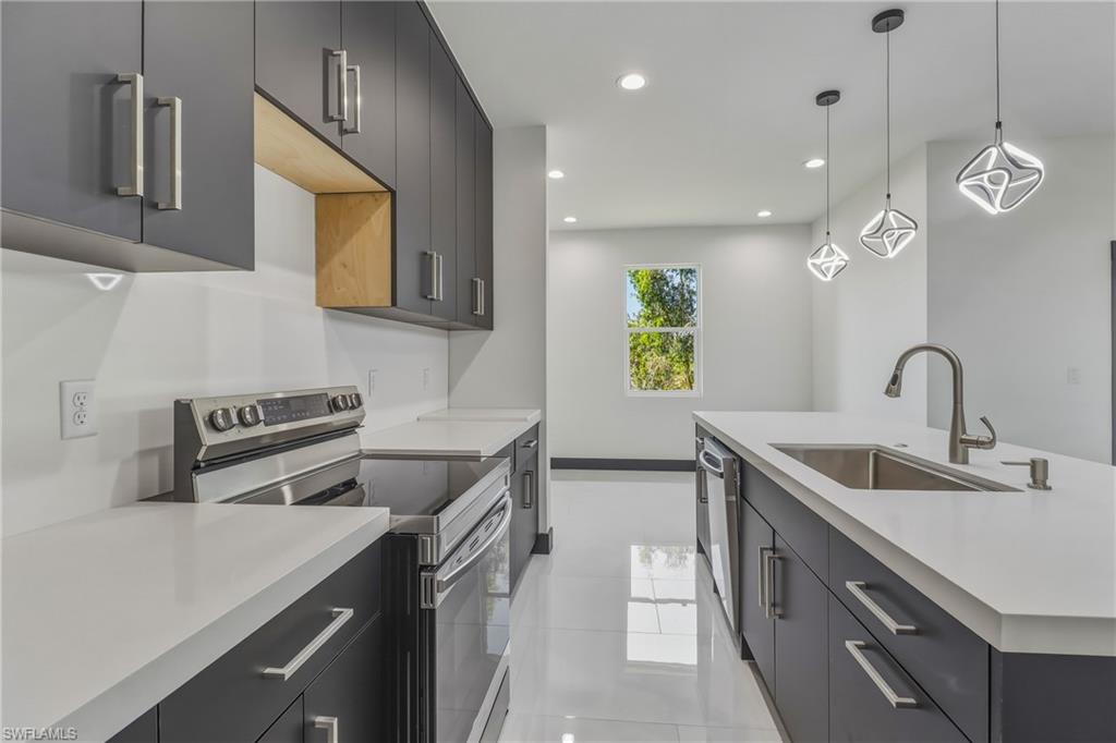 Kitchen featuring stainless steel appliances, modern cabinets, hanging light fixtures, an island with sink, and dark cabinets