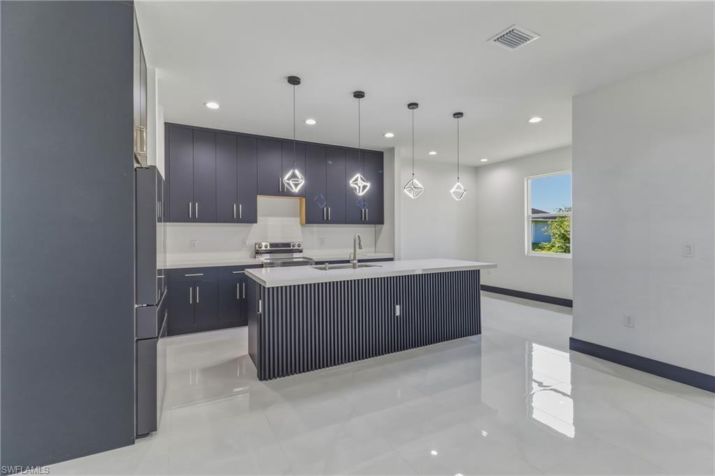 Kitchen with modern cabinets, a kitchen island with sink, freestanding refrigerator, hanging light fixtures, and electric stove