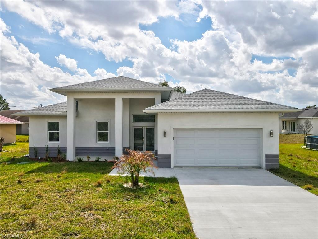 Prairie-style home with a front lawn, an attached garage, stucco siding, and driveway