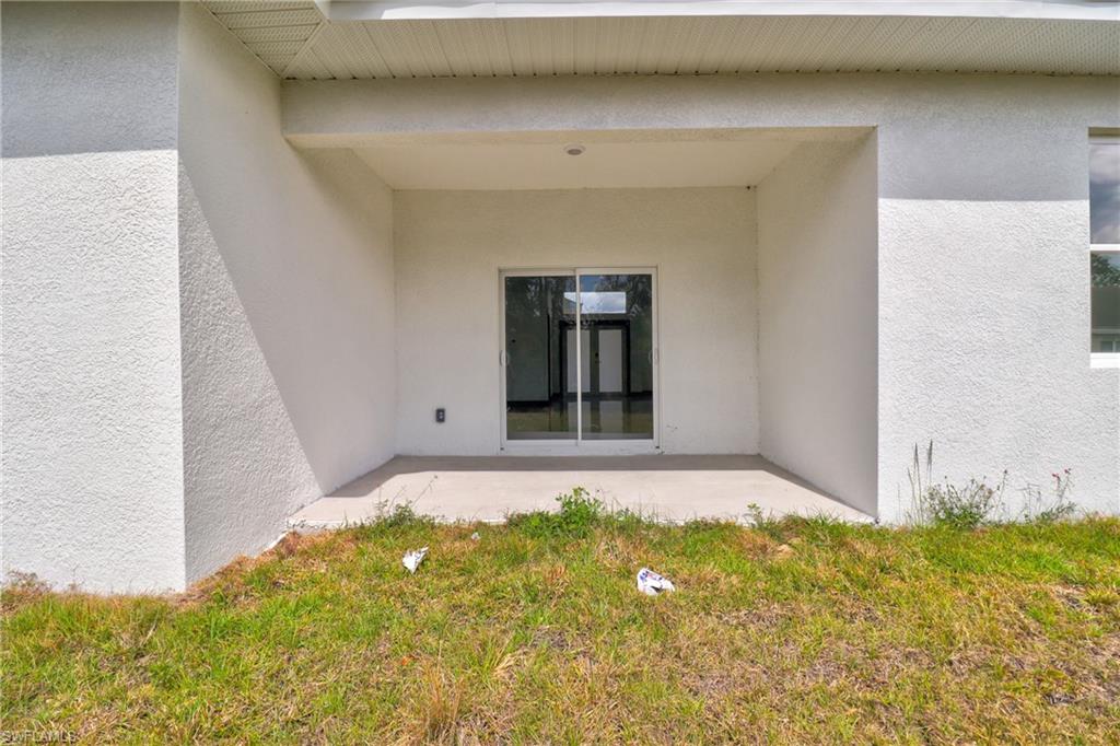 View of exterior entry with stucco siding, a patio, and a lawn