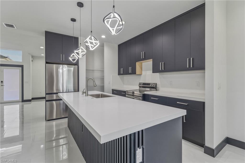 Kitchen with stainless steel appliances, dark cabinets, a center island with sink, modern cabinets, and pendant lighting