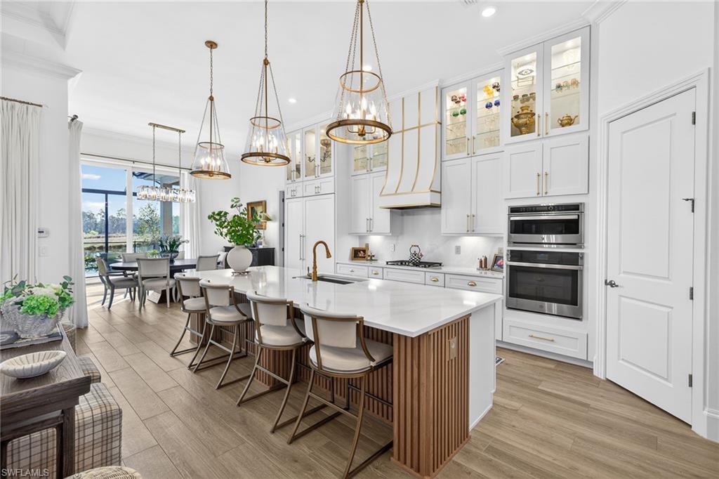 Kitchen with white cabinetry, glass fronted cabinets, a breakfast bar area, an island with sink, and light wood finished floors