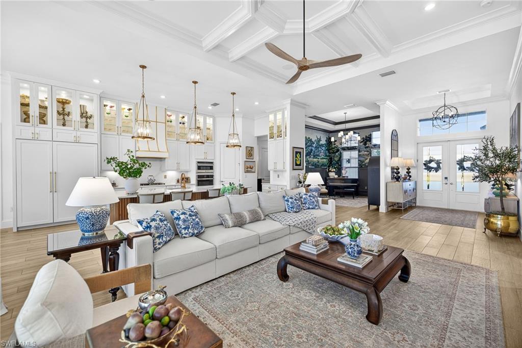 Living room with light wood-style floors, coffered ceiling, a chandelier, crown molding, and a ceiling fan
