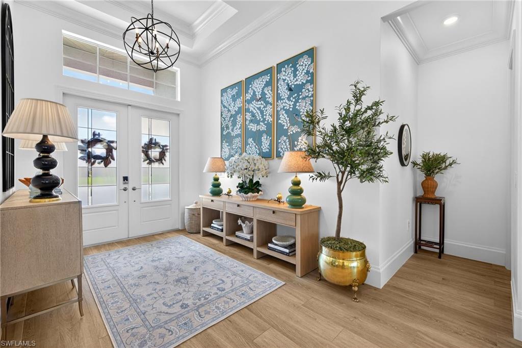 Foyer featuring french doors, ornamental molding, light wood-type flooring, hanging lights, and a high ceiling