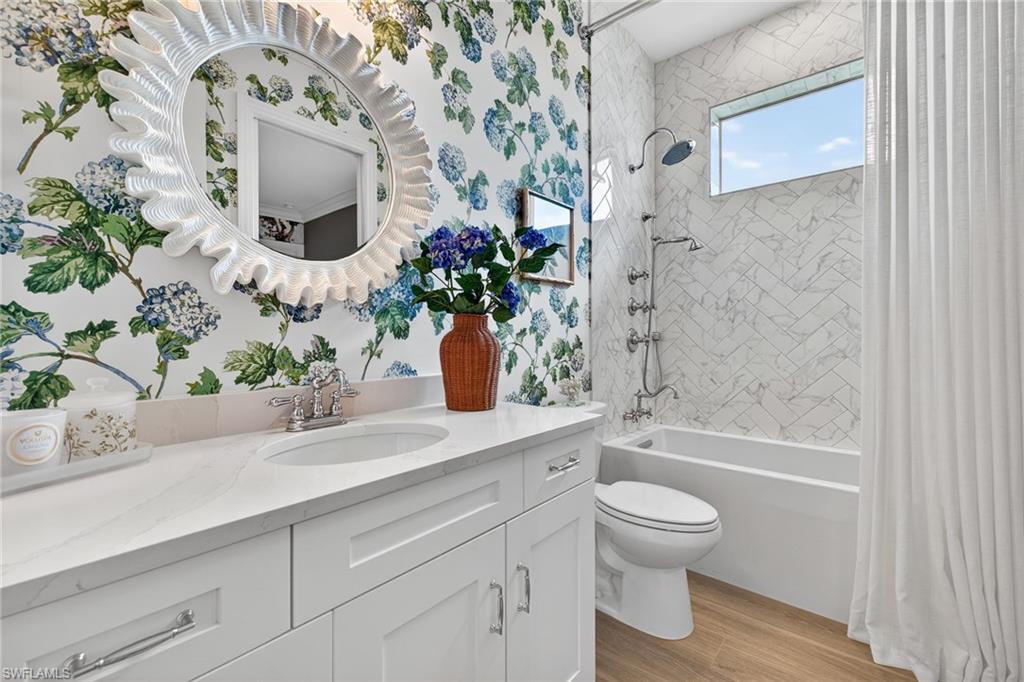 Full bathroom featuring vanity, shower / tub combo, light wood-style flooring, and wallpapered walls