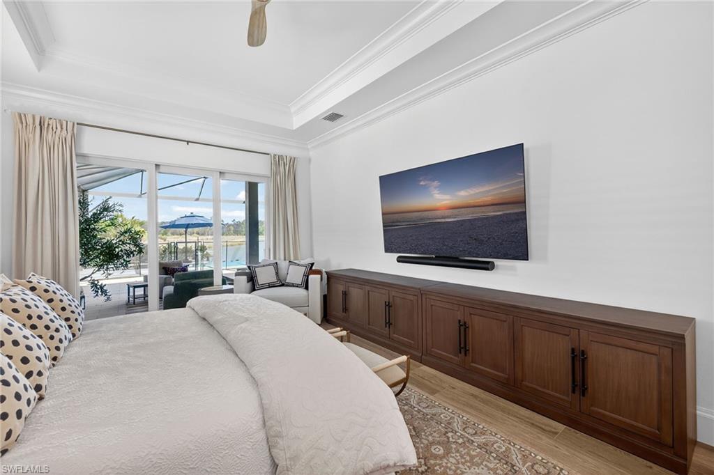 Bedroom with light wood-style floors, access to exterior, a ceiling fan, a raised ceiling, and crown molding