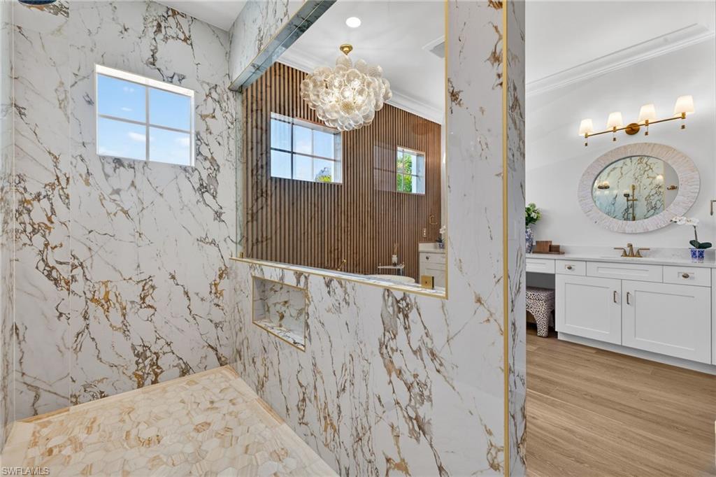 Full bathroom with vanity, a marble finish shower, hanging lights, crown molding, and light wood-style flooring