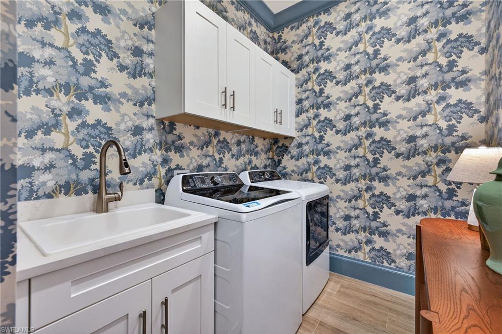 Laundry area featuring wallpapered walls, light wood finished floors, washer and clothes dryer, and cabinet space