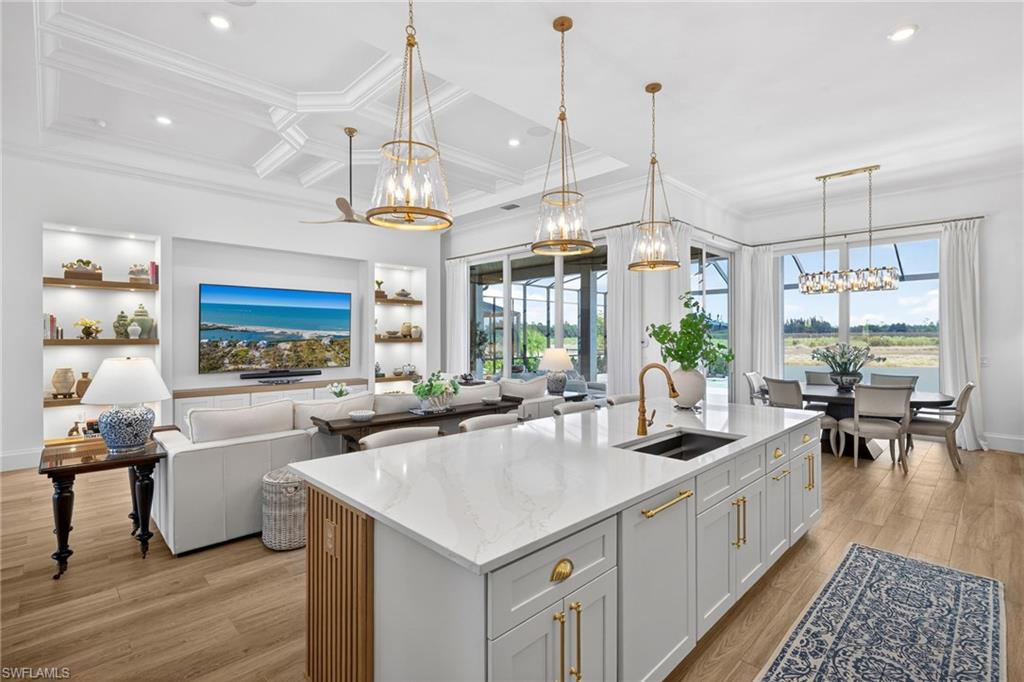 Kitchen with a chandelier, light stone counters, an island with sink, light wood finished floors, and open floor plan