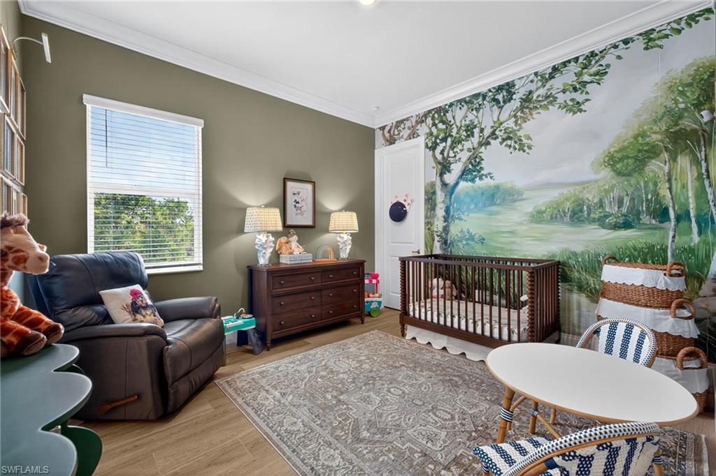 Bedroom with a nursery area, light wood finished floors, and crown molding