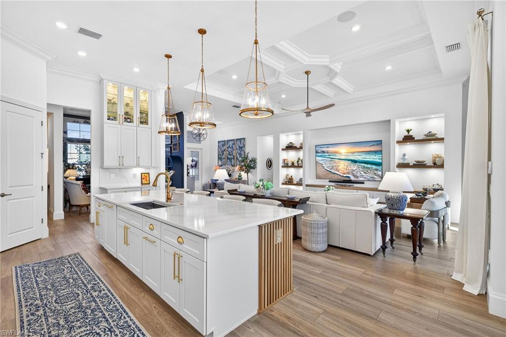 Kitchen with white cabinetry, open floor plan, glass fronted cabinets, a center island with sink, and light stone countertops