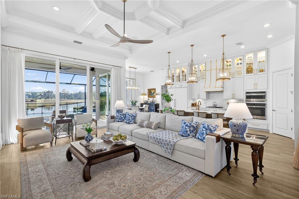 Living room featuring coffered ceiling, ornamental molding, a ceiling fan, suspended lighting, and a water view
