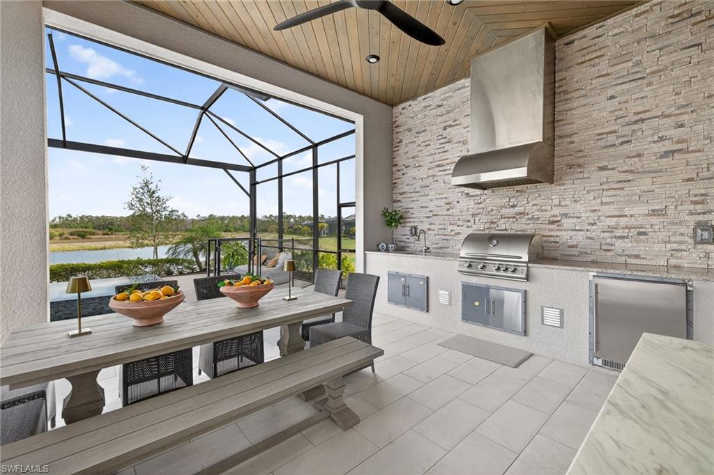 View of patio / terrace with a sunroom, an outdoor kitchen / dining area, glass enclosure, a water view, and a ceiling fan
