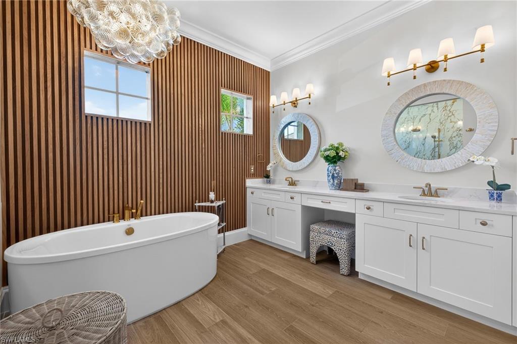 Bathroom with double vanity, crown molding, light wood-type flooring, a freestanding tub, and hanging lights