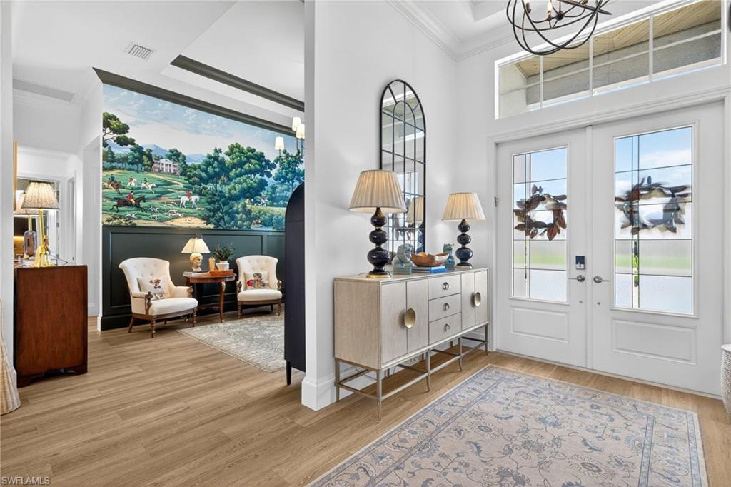 Foyer with light wood-style flooring, ornamental molding, a high ceiling, french doors, and a chandelier