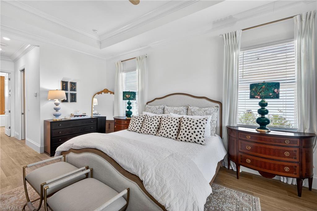 Bedroom featuring light wood-style flooring, a raised ceiling, crown molding, and ceiling fan