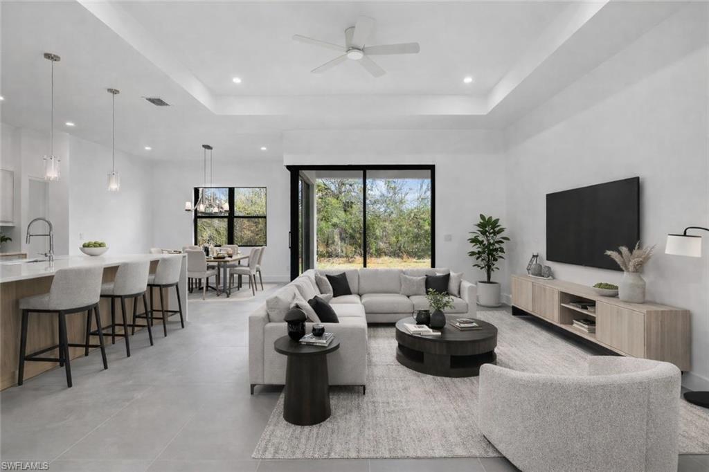 Living room with a tray ceiling, ceiling fan, and recessed lighting. This photo is virtually staged.