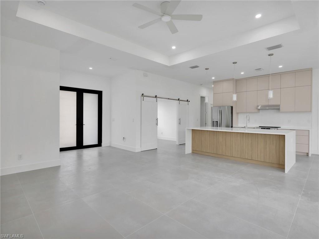 Kitchen featuring a barn door, modern cabinets, a tray ceiling, a center island with sink, and open floor plan