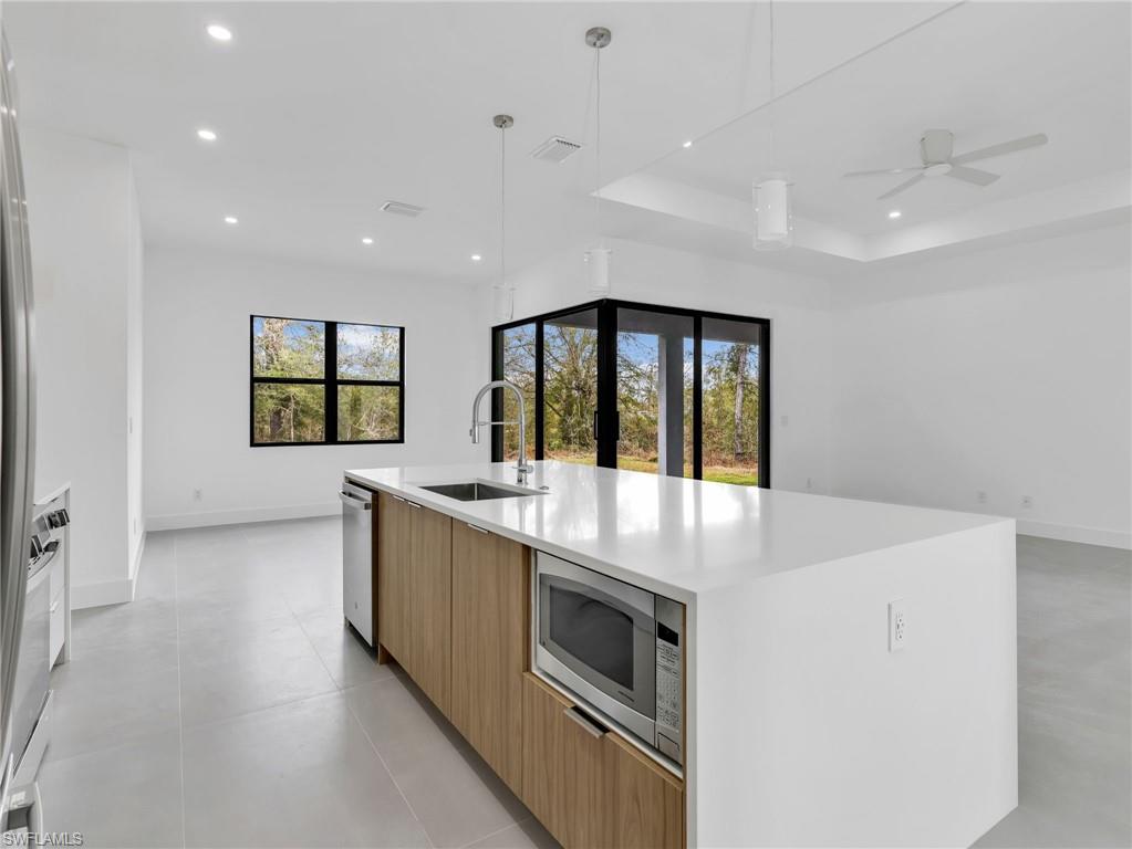 Kitchen with modern cabinets, light stone countertops, a large island with sink, stainless steel appliances, and a ceiling fan