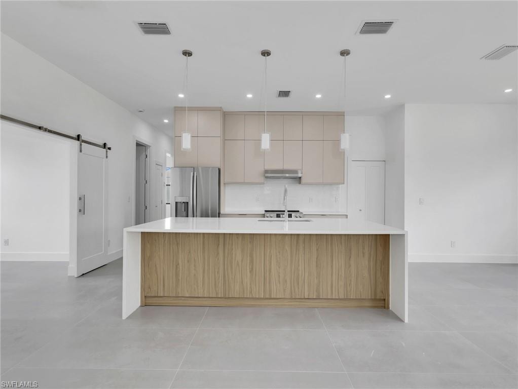 Kitchen with a spacious island, hanging light fixtures, a barn door, light stone counters, and stainless steel fridge with ice dispenser
