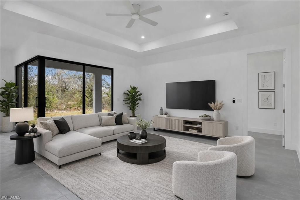 Living area featuring concrete floors, a tray ceiling, ceiling fan, and recessed lighting. This photo is virtually staged.