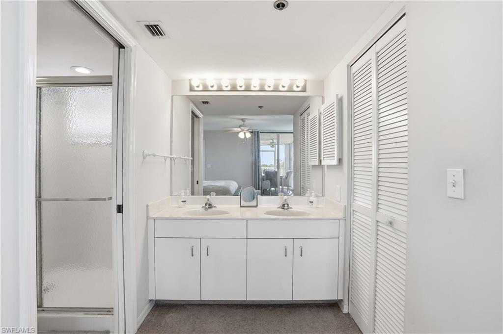 Full bathroom with a closet, double vanity, ensuite bath, a stall shower, and a ceiling fan
