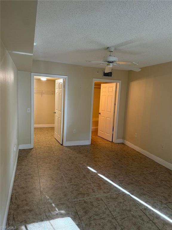 Unfurnished bedroom featuring a spacious closet, a textured ceiling, ceiling fan, and light tile patterned floors