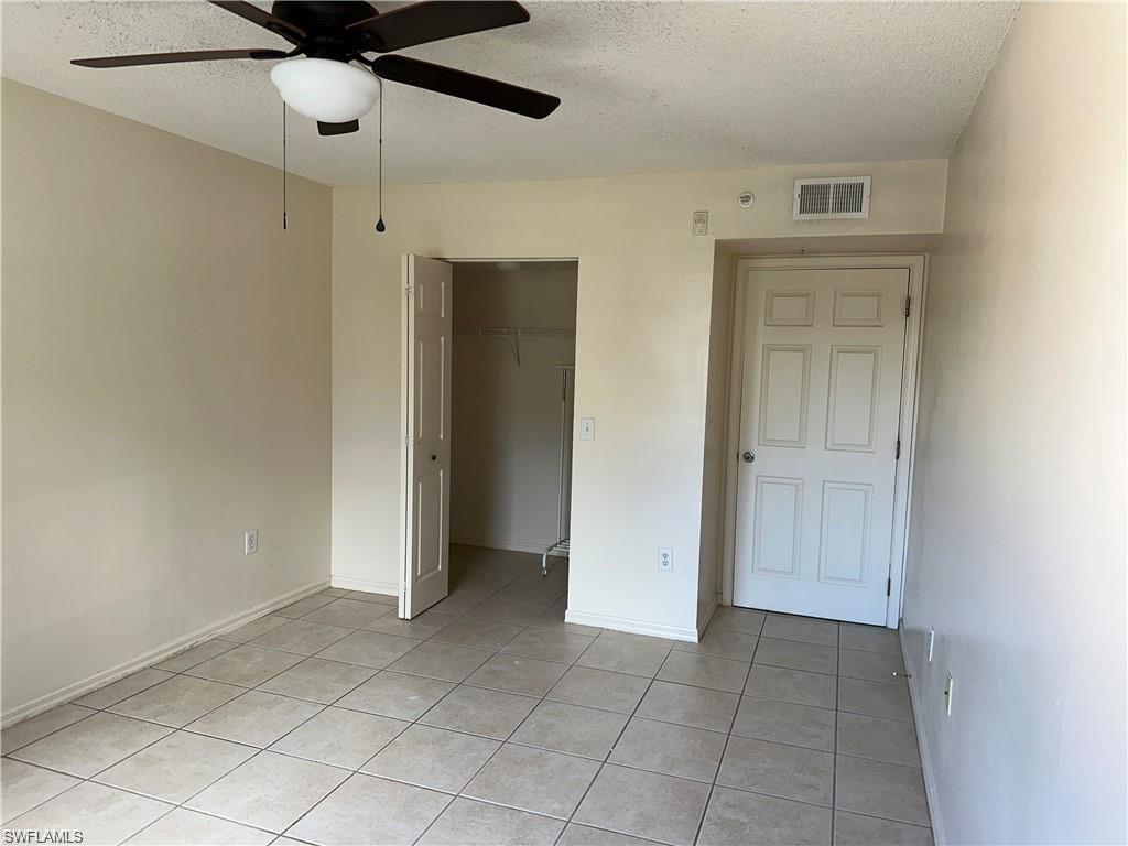 Unfurnished bedroom with a textured ceiling, ceiling fan, a closet, and light tile patterned floors