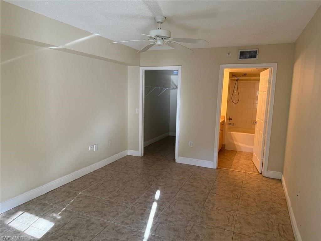 Unfurnished bedroom with a walk in closet, ceiling fan, connected bathroom, a textured ceiling, and light tile patterned flooring
