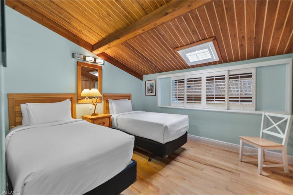 Bedroom with light wood finished floors, vaulted ceiling with beams, and wooden ceiling