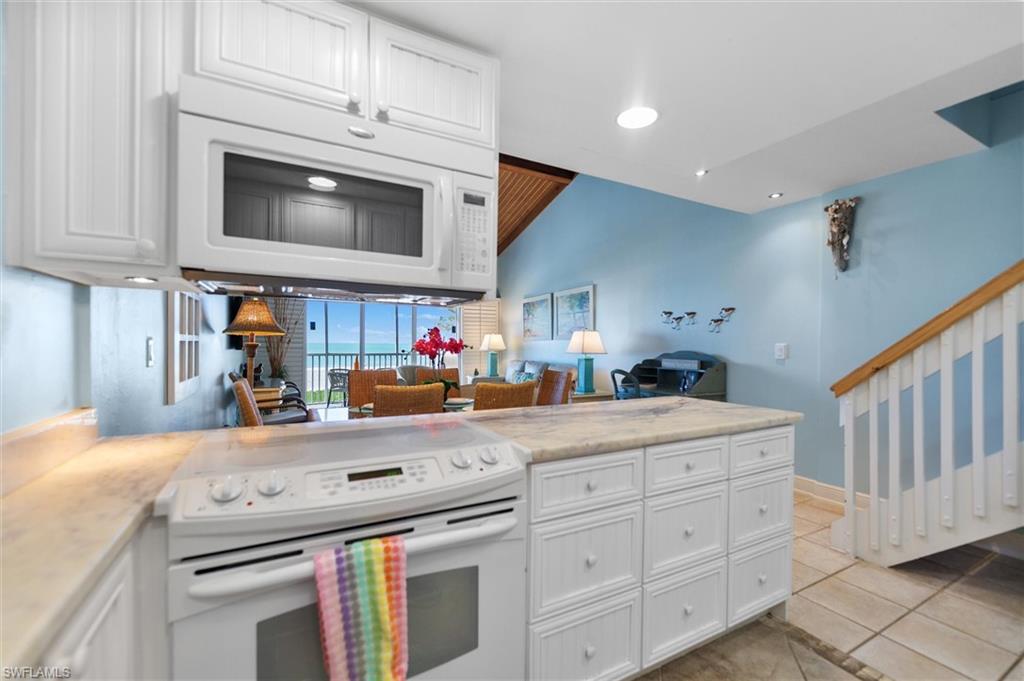 Kitchen with white appliances, white cabinets, a peninsula, open floor plan, and light tile patterned floors