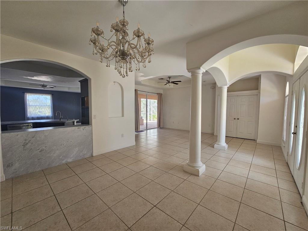 Unfurnished living room with a wealth of natural light, ornate columns, light tile floors, and ceiling fan with notable chandelier