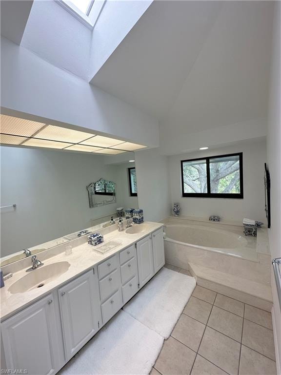 Full bathroom featuring a skylight, light tile patterned floors, a garden tub, double vanity, and vaulted ceiling