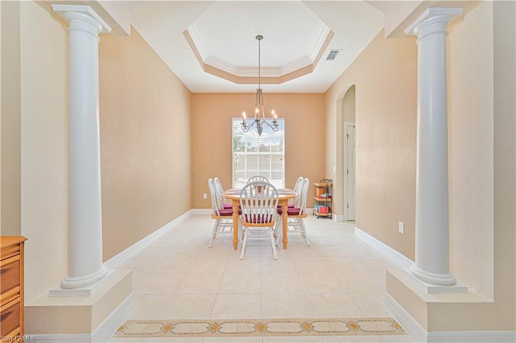Dining room with ornate columns, a raised ceiling, ornamental molding, light tile patterned floors, and a chandelier