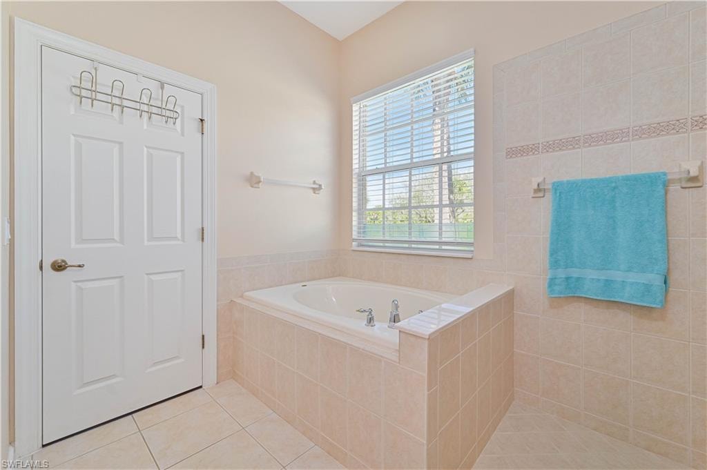 Full bath featuring light tile patterned flooring, a garden tub, and tile walls