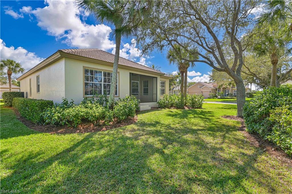 Rear view of property featuring a lawn, a sunroom, stucco siding, and a tiled roof