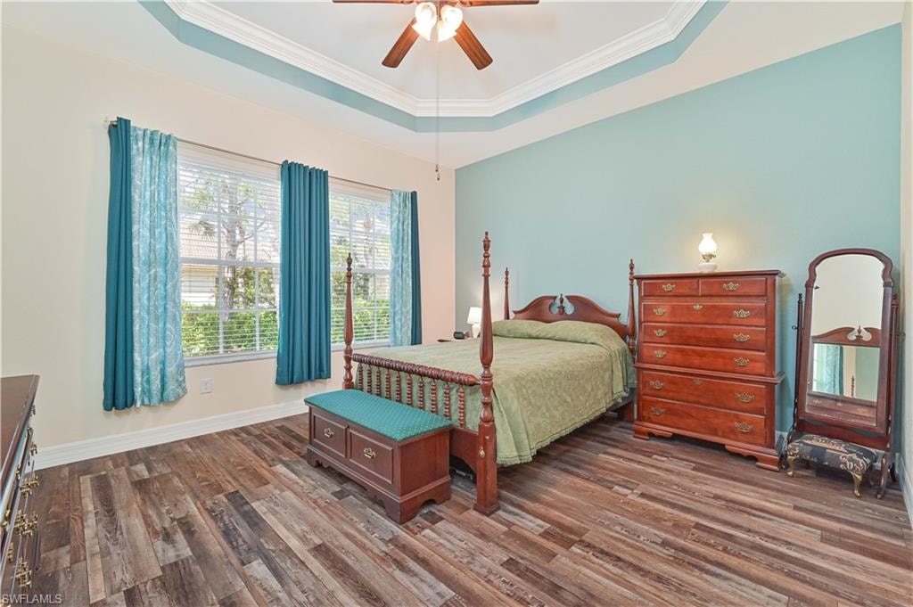 Bedroom with a raised ceiling, dark wood-type flooring, a ceiling fan, and crown molding