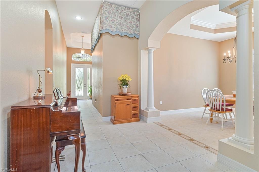 Foyer with light tile patterned floors, ornate columns, arched walkways, a chandelier, and a raised ceiling