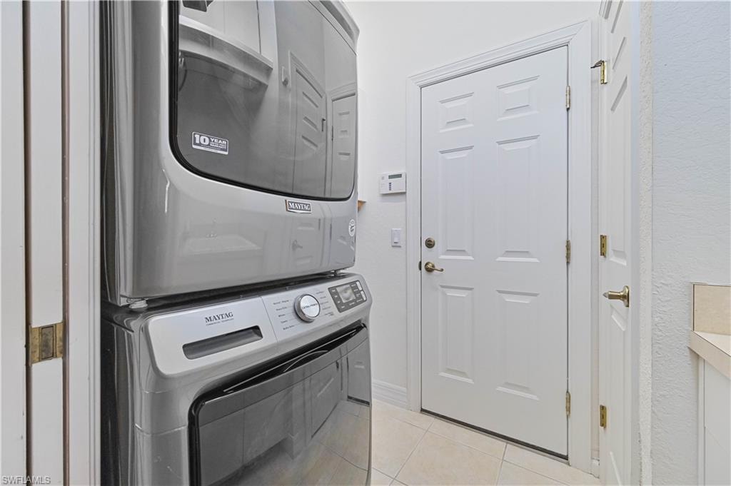 Laundry area with stacked washer / drying machine and light tile patterned flooring