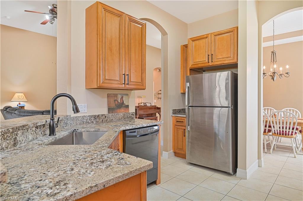 Kitchen featuring light stone counters, freestanding refrigerator, ceiling fan, black dishwasher, and light tile patterned floors
