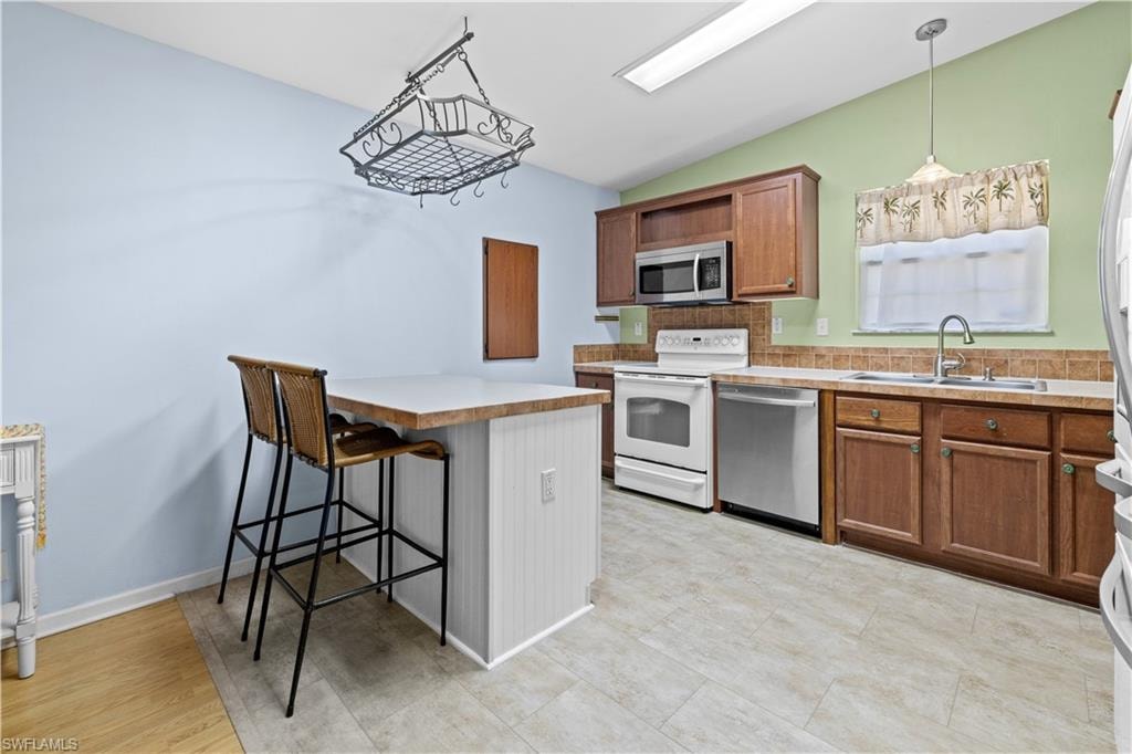 Kitchen featuring a breakfast bar, stainless steel appliances, light countertops, backsplash, and vaulted ceiling