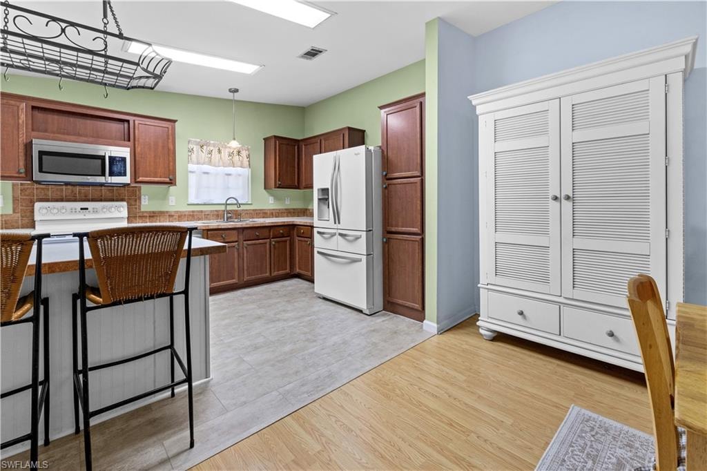 Kitchen featuring white appliances, light wood-style floors, pendant lighting, a kitchen breakfast bar, and light countertops