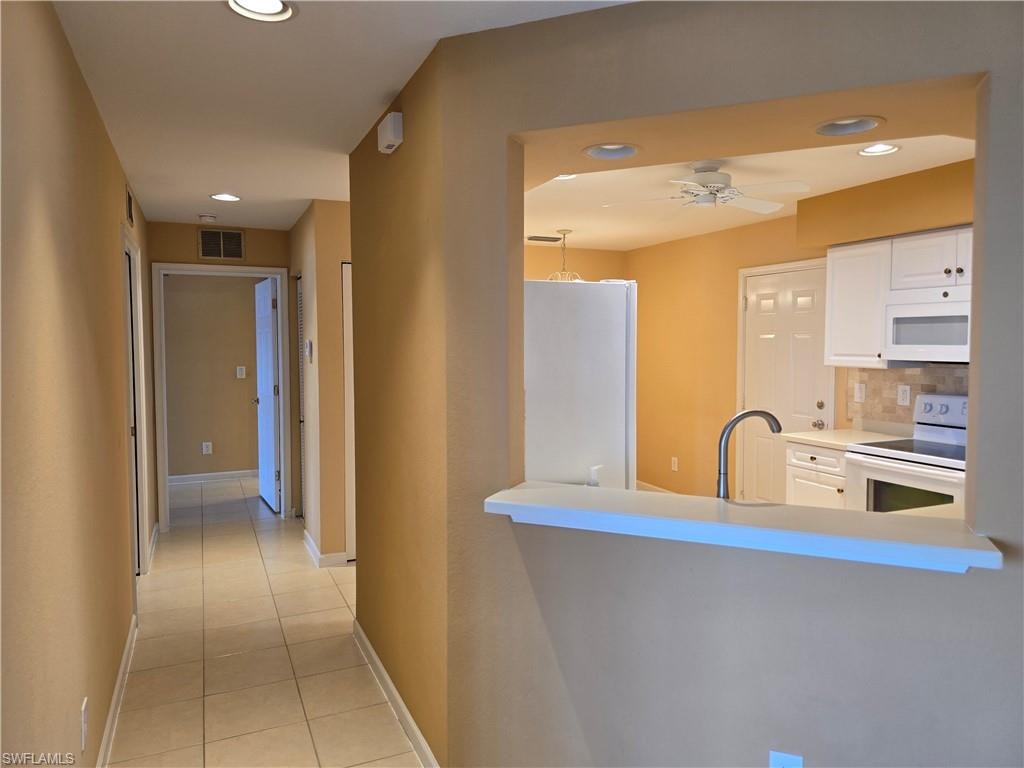 Kitchen featuring white appliances, light countertops, light tile patterned floors, white cabinetry, and a ceiling fan