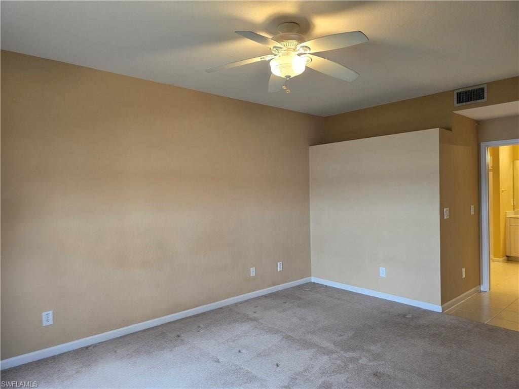 Large master bedroom with light colored carpet and a ceiling fan