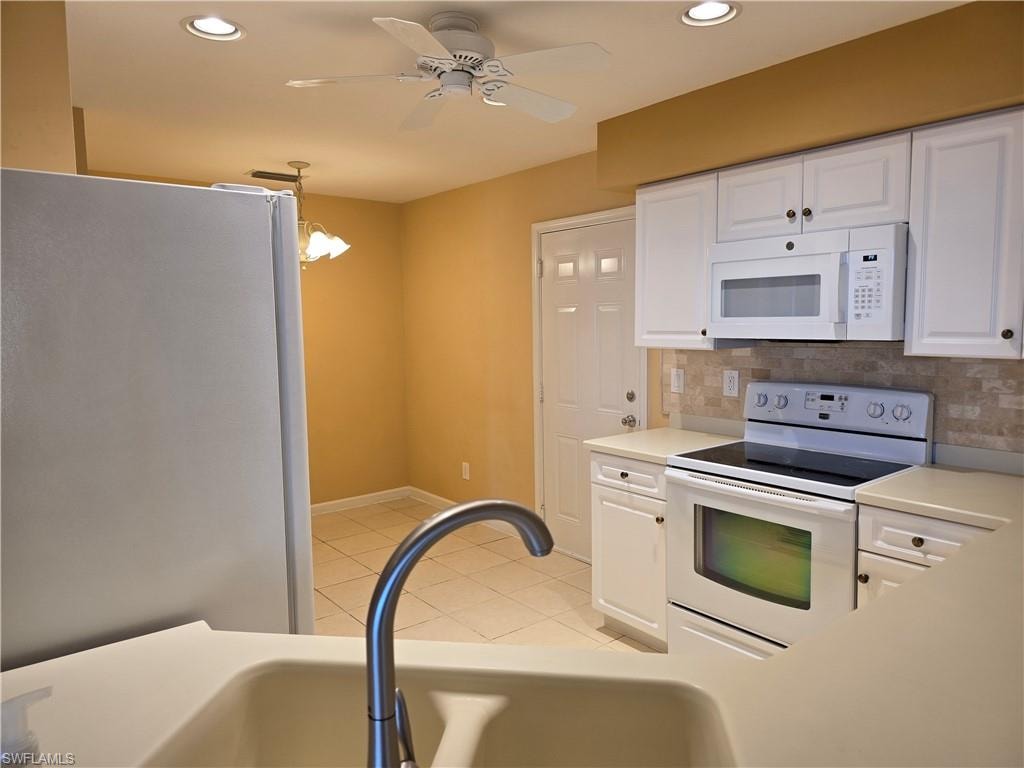 Kitchen featuring white cabinets, white appliances, light countertops, a ceiling fan, and decorative backsplash