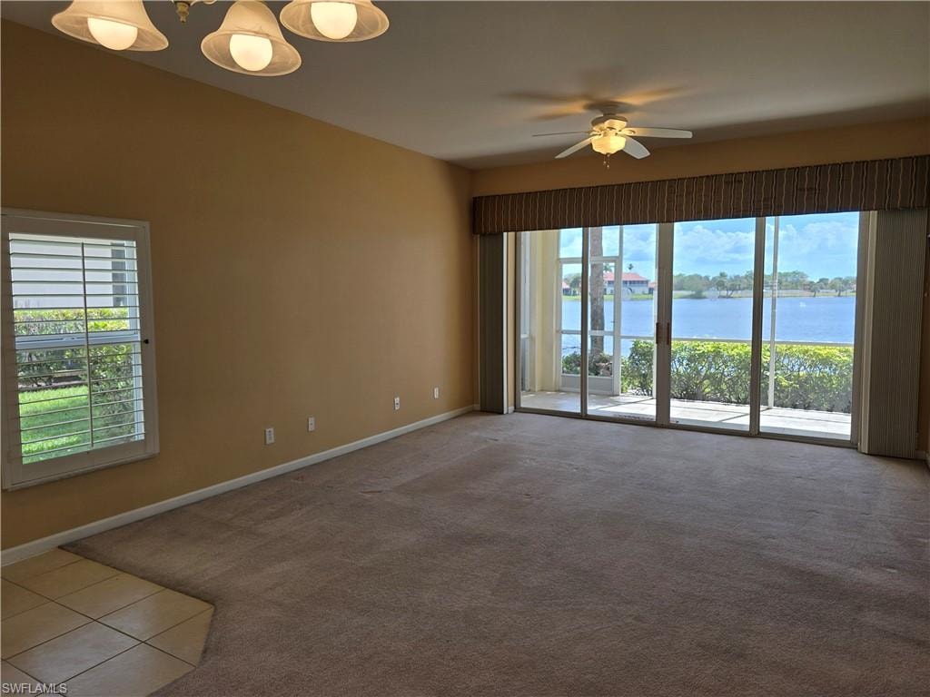 Living room featuring a ceiling fan, light colored carpet, a lake view, and light tile patterned floors