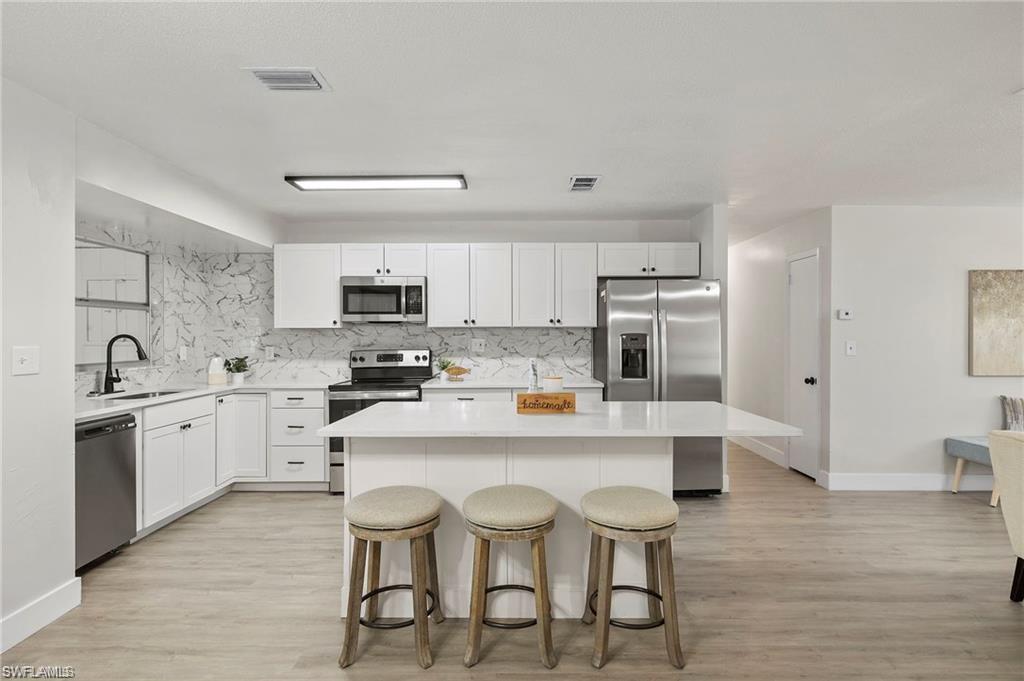Kitchen with stainless steel appliances, a kitchen bar, a center island, and light wood finished floors