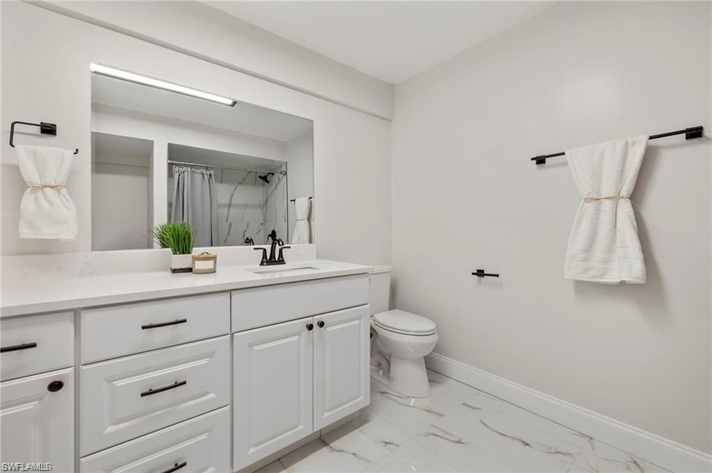 Full bath featuring curtained shower, vanity, and light marble finish floors