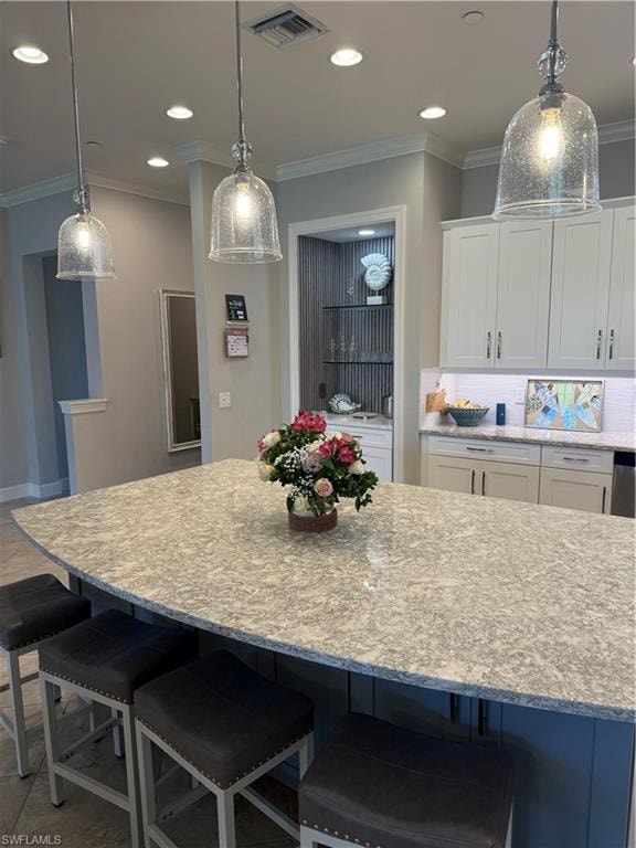 Kitchen with a breakfast bar, decorative light fixtures, crown molding, light stone countertops, and white cabinets